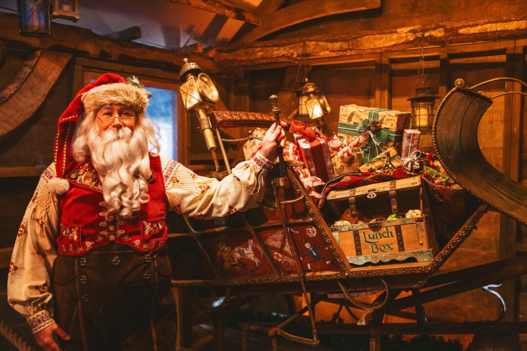 Image of Santa standing next to a sleigh filled with wrapped parcels.
